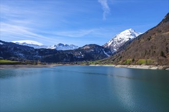 Lake Lungern surrounded by snow-capped mountains and green hills under a blue sky, Lungern,