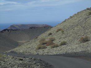 Winding road through a barren volcanic landscape with rocky hills and distant ocean, barren