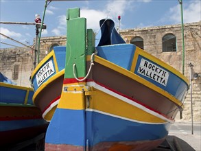 Bow of a colourful boat with the inscription ROCKY II VALLETTA, under a clear blue sky, many