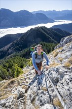 Hiker on via ferrata to Ettaler Manndl, view over mountain landscape and sea of clouds, high fog in