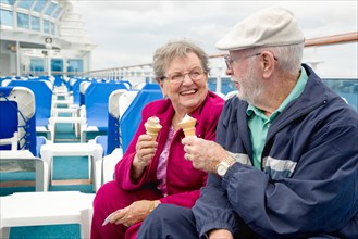 Happy senior adult couple enjoying ice cream on the deck of a luxury passenger cruise ship