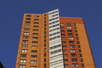 Modern high-rise brick building with many glass windows under a clear blue sky, skyline of a modern