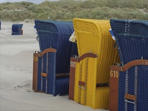 A row of colourful beach chairs on the sandy beach under a cloudy grey sky, colourful beach chairs