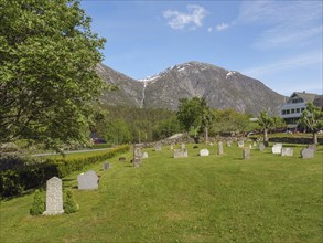 Large cemetery on a green meadow with mountains in the background on a sunny day, gravestones with