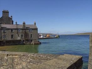 Historic stone wall and houses overlooking the sea and harbour with boats, old stone house by the