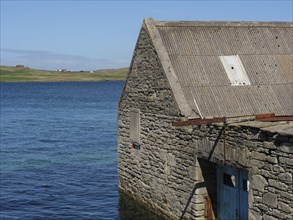 Stone clad building on the water's edge with sea and sky in the background, old stone house on the