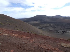 Volcanic landscape with red soil and hills under a slightly cloudy sky, barren landscape with