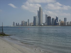A sandy beach with a view of modern skyscrapers of a city by the sea under a cloudy sky, impressive