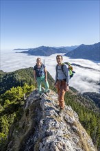 Two hikers at Ettaler Manndl, view over mountain landscape and sea of clouds, high fog in the