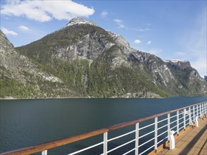Ship deck in front of impressive mountain landscape with clear sea under blue sky with few clouds,