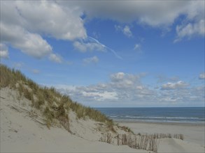 View of the beach with sand dunes and the sea under a blue cloudy sky, dunes on an island with a