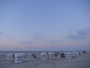 A peaceful scene on the beach with white and striped beach chairs during dusk, setting sun on a
