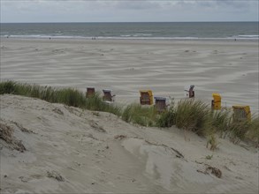 Deserted beach with beach chairs under a cloudy sky and gentle dunes, colourful beach chairs on the