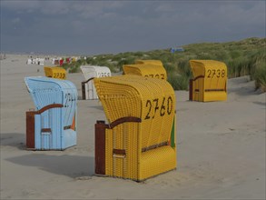 View of colourful beach chairs in front of cloudy sky, some baskets in the sand with dune grass,