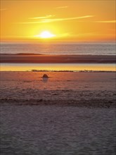 Sunset over the sea with a calm beach and a lonely stone in the foreground, beautiful sunset on the