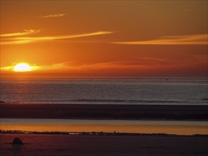Bright sunset over the sea, dark silhouettes and calm water on the beach, beautiful sunset on the