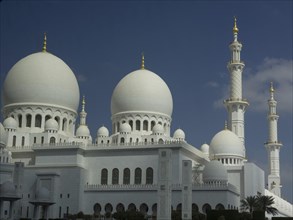 White shining mosque with several domes and high minarets under a blue sky, large mosque with white