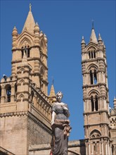 Historic cathedral with detailed towers and a central statue, under a bright blue sky, two red