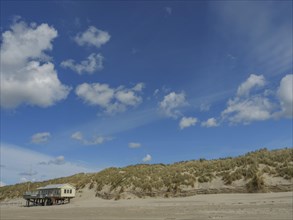 Beach view with grassy dunes and a house under a cloudy sky, clouds on the beach with dunes by the