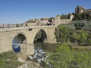 Stone bridge over the river, old city with cathedral in the background, many trees and blue sky,