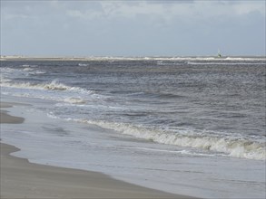 Waves rolling on a long, deserted beach under a cloudy sky, waves on a beach, sunny day with clouds