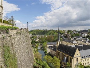 View of historic city wall, river and church in a green, hilly landscape under a cloudy sky, old