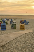 Colourful beach chairs on a quiet beach at sunset with a wooden walkway and soft sand, many