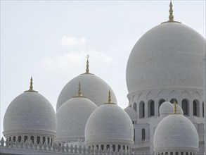 Detailed view of several white domes of a mosque with golden tips under a blue sky, beautiful