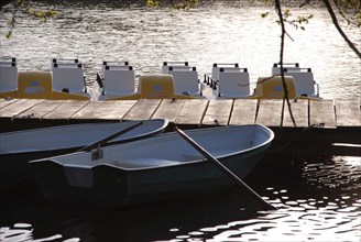 Wooden jetty with rowing boats in the foreground and pedal boats in the background on a calm lake