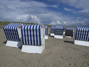 Blue and white beach chairs on the beach in front of dunes and a cloudy sky, blue and white striped