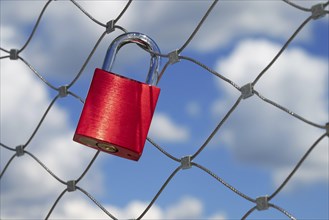A red love lock hangs on a bridge railing in front of a blue sky with clouds