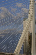 Close-up of a modern cable bridge in front of a skyscraper under a cloudy sky, skyline of a modern