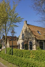 Cosy brick houses with red roofs, lampposts, green hedges and lush trees, historic houses in a