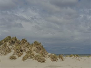 Sand dunes with grass under an overcast sky, dune with dune grass and a boat by the sea, clouds on