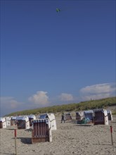Beach with several beach chairs, flying kite and dunes in the background, dunes and beach at the