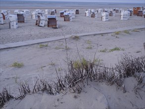 A quiet beach with white and striped beach chairs and sand dunes in the twilight, setting sun on a