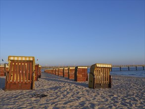 Beach chairs on a sunny beach with blue sky and calm sea, in the background a pier, beach chairs in