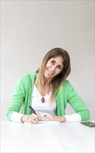 An attractive mid-adult woman is writing in her notebook while she looks at the camera