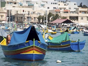 Colourful fishing boats in the harbour, partly covered with tarpaulins, in front of a coastal town