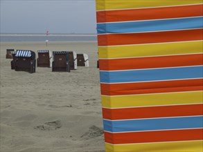 An empty beach with colourful stripes in the foreground and beach chairs in the background, beach