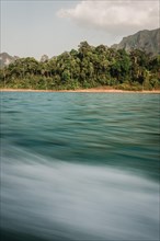 Moving water in front of a picturesque coastline with forest in the background. Khao Sok National