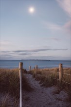Path through the dunes to the sea at sunset. Calm sea, moonlight, island. Blue hour & footprints in