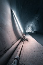An urban tunnel with industrial pipes and lighting, concrete walls and a sterile, futuristic