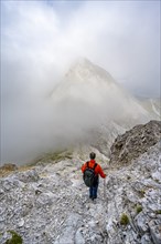 Mountaineer descending on a rocky mountain path, cloudy mountain peak, descent from the summit of