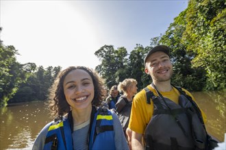 Happy tourists in a rowing boat on the Tortuguero River, watching animals in the rainforest,