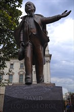 Bronze statue of David Lloyd George with gesturing hand in front of a historic building, London,