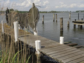A wooden jetty leads out into the water, lined with fishing nets and surrounded by calm lake shores