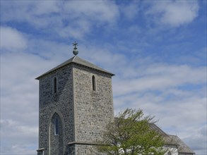 Stony church tower in front of a clear sky, partly hidden by a tree, old stone church and many