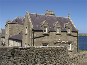 Stone building with skylights behind a stone wall on a clear day by the sea, old stone house by the