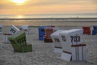 White, red and green beach chairs on a sandy beach at sunset, many colourful beach chairs on a warm